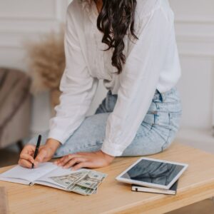 Person writing in a notebook with cash on the table